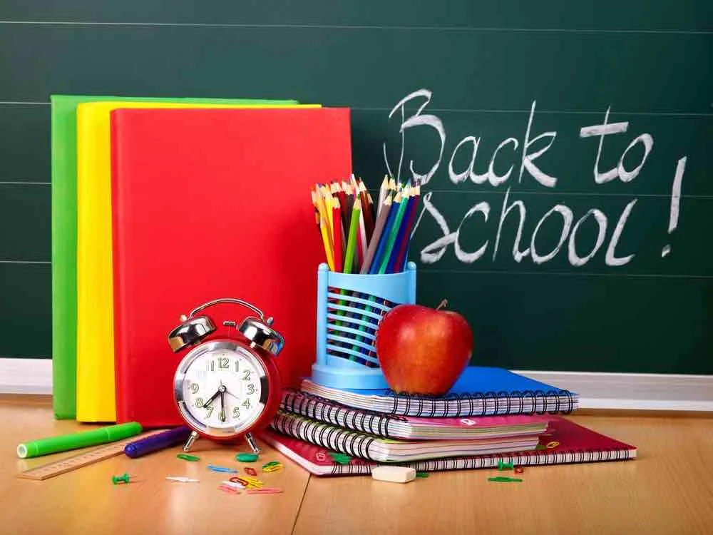 Fournitures scolaires devant un tableau avec "Back to School" écrit dessus.